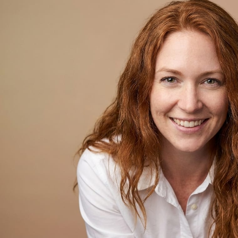 The same person against a muted earth-tone gradient backdrop, lit with a soft key light, a relaxed lean toward the camera.