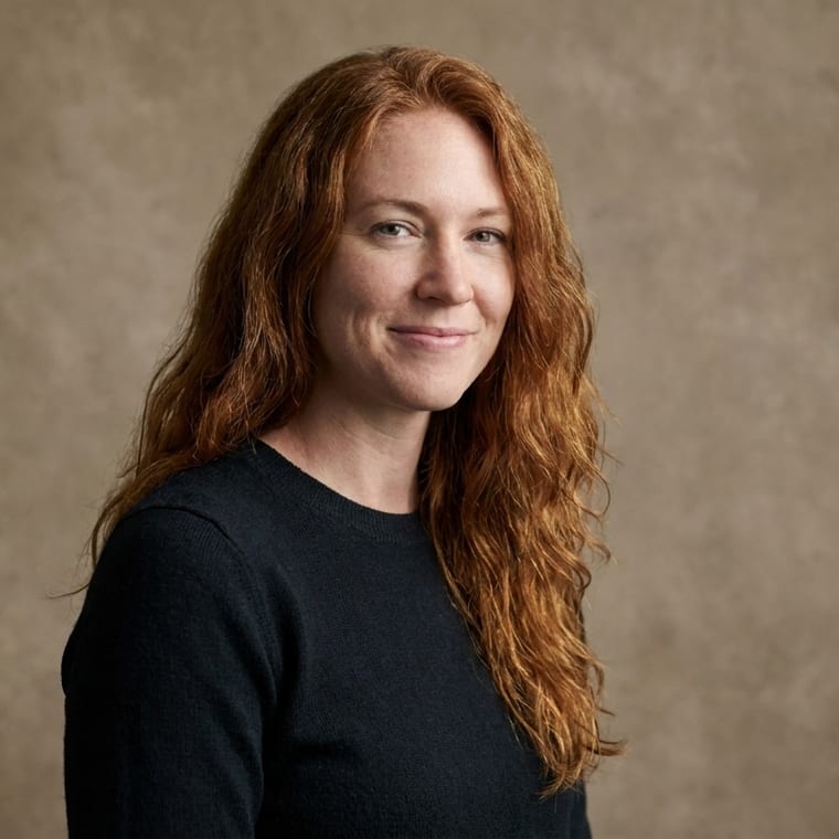 The same person against a hand-painted warm canvas backdrop, lit by window daylight, body turned three-quarters to the camera.