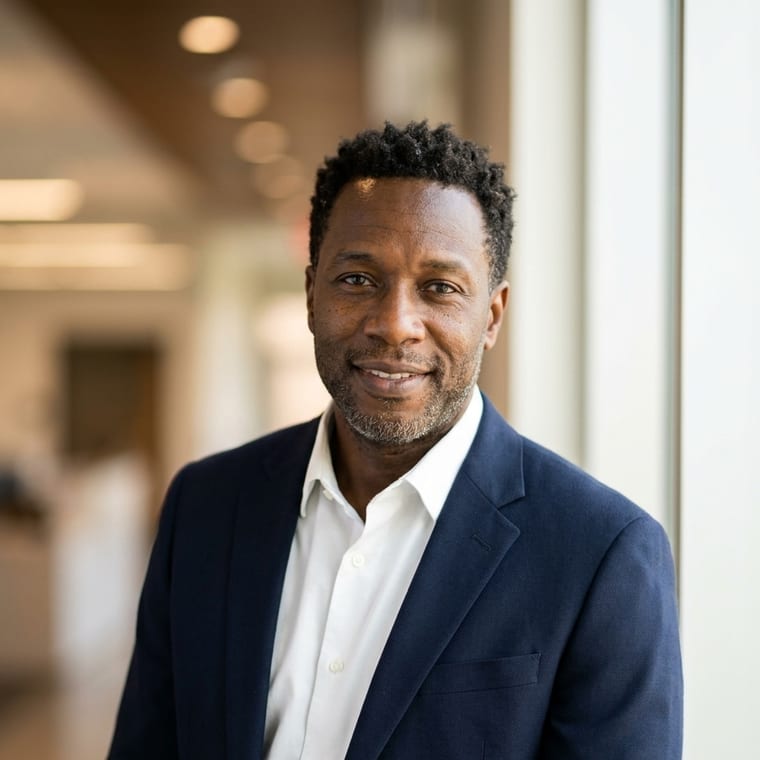 The same agent with a softly blurred office interior behind them, lit by warm window daylight, a relaxed lean toward the camera.
