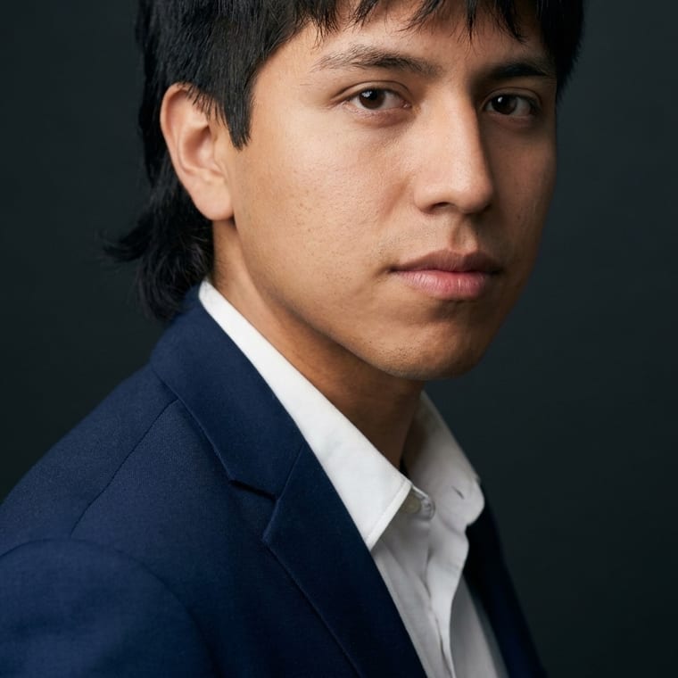 Young man in navy blazer against a dark studio background