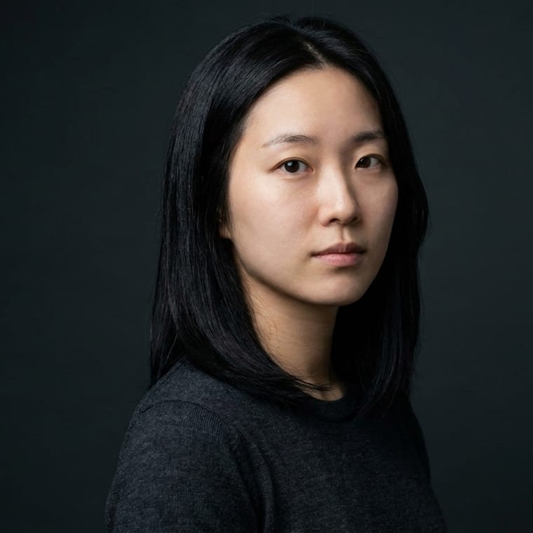 A portrait on a charcoal backdrop lit with a Rembrandt key light, body turned three-quarters to the camera, tight crop.